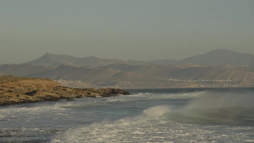 Small coastal community among mountains along the coast as waves roll in to shore