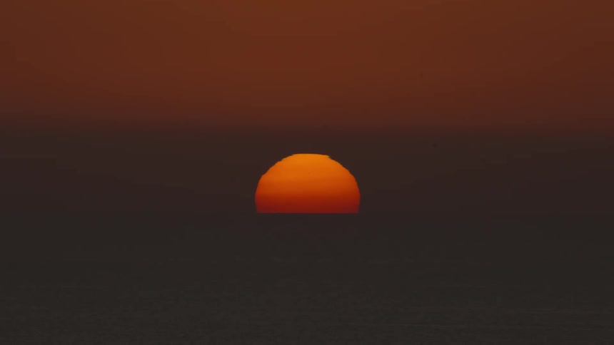 Setting sun glows over the water on the horizon in a deep dark red sky