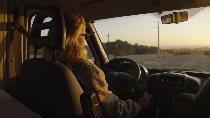 Woman shifts while steering through a turn onto a highway heading toward the red tinted horizon