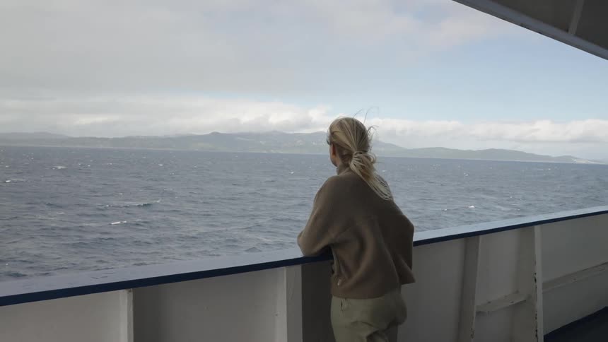 Woman stares into the ocean while standing on a ship deck in daytime