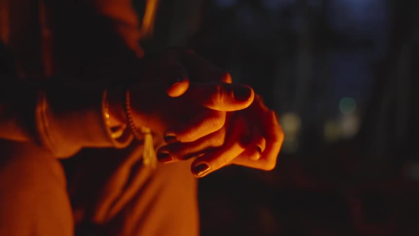 A woman sits by the campfire at night