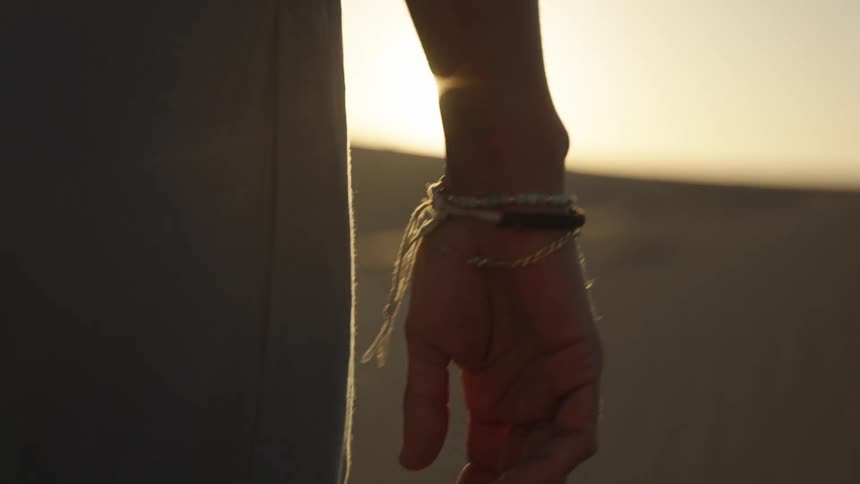 A man stands with his back to the camera facing a hill with the sun peeking over the horizon