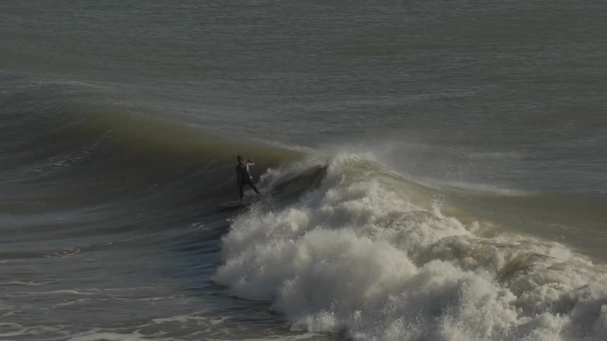 A group of surfers is riding large waves while others wait in the background