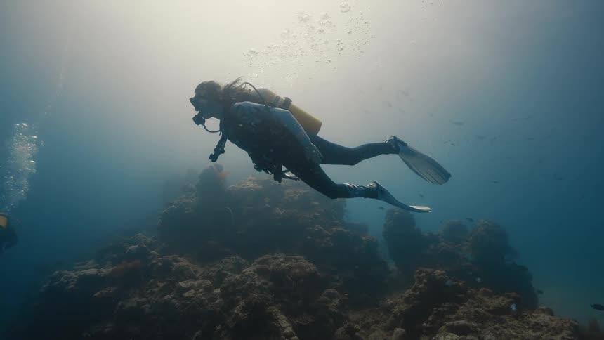 A sea diver wearing diving gear swims above the ocean floor