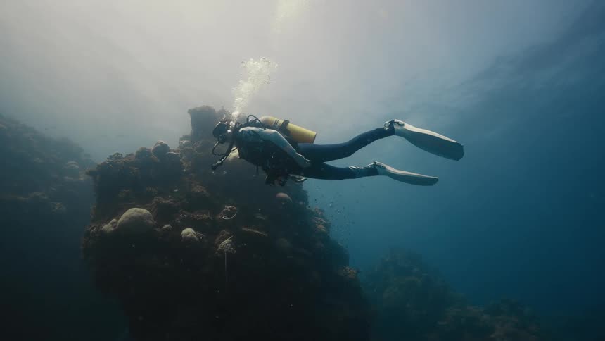 A man in full diving gear is swimming underwater near a reef