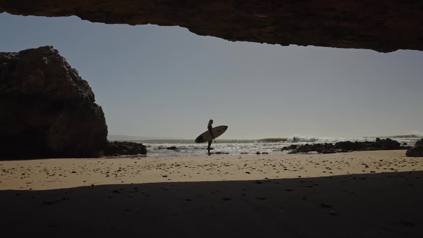 A lady stands by the sea with a surfboard on a sunny day