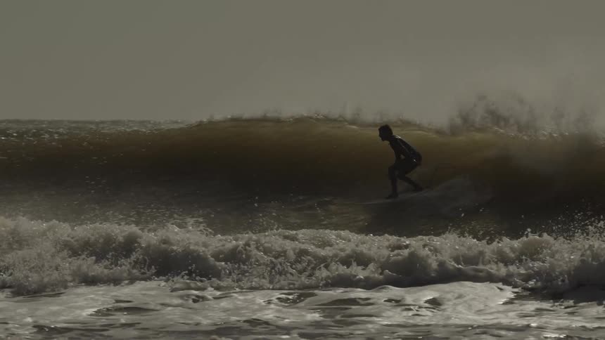 A surfer rides a powerful wave amid crashing surf near the shore