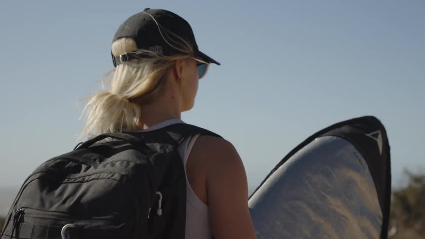 A woman holding a surfboard and walking toward the beach