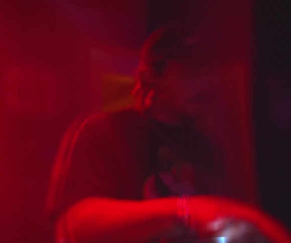 A man inside a house at a party playing electronic music under red lighting