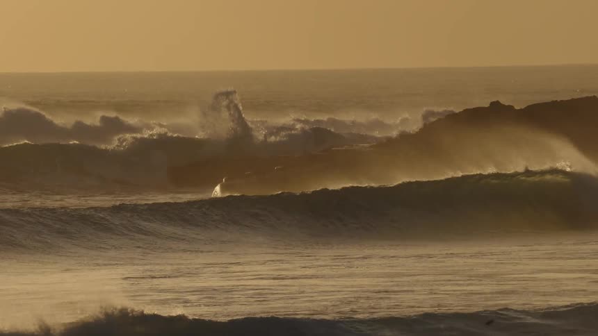 Waves flowing across stormy seas splash against the coast under a red sky