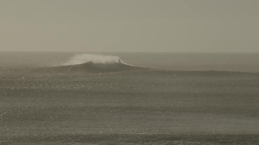 Water ripples and a wave splashes as it rolls in to shore on a rainy day