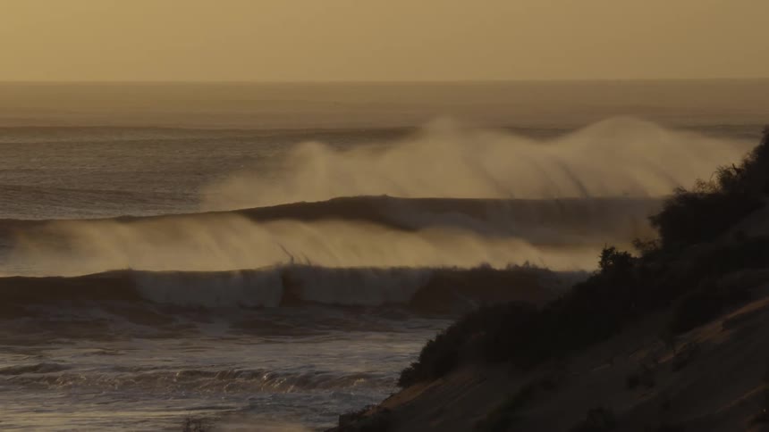 Waves roll into shore at the promontory under a hazy sunset sky