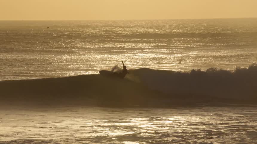 A man surfing a wave while other people swim in the ocean behind him