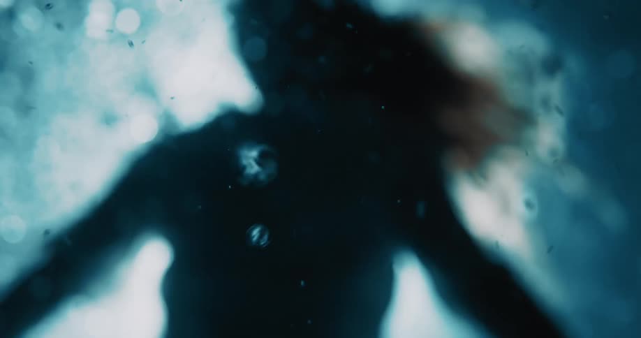 A shadowy figure is submerged underwater with rising bubbles and a deep blue abstract tone