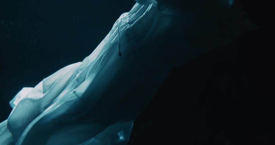 Woman wearing a white dress floats face up in dark water