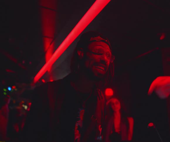 Dj in a nightclub talking and other people in the background dancing