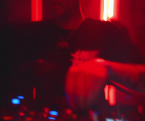 Under vivid red lighting hands actively adjust the controls of a mixing console capturing the energy of a dj in motion