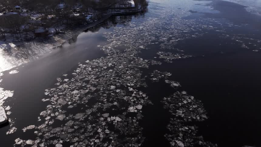 The river near the city has ice floating by the shore