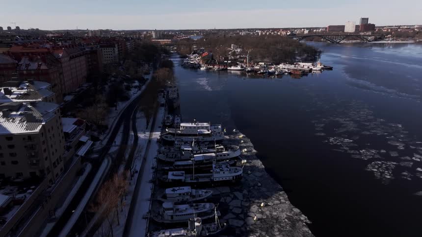 Floating ice surrounds watercraft sitting at dock near a large city on a winter day