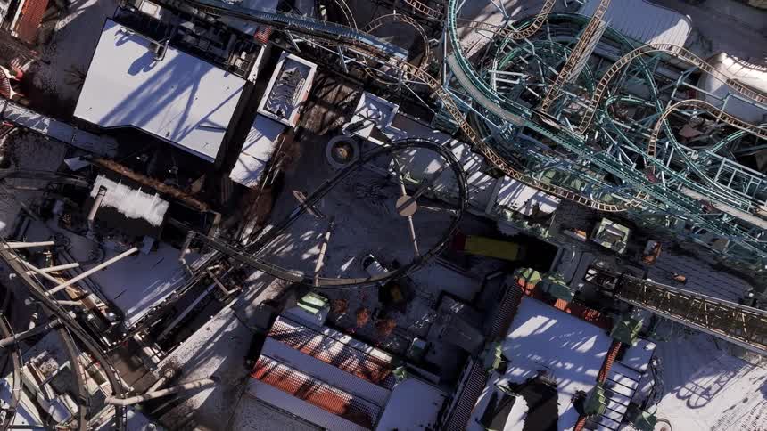 Snow covers the area surrounding a roller coaster located in a waterfront amusement park on a winter day