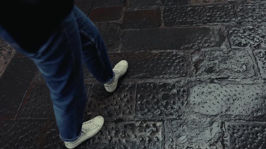 Person in jeans and white sneakers walking on a wet sidewalk