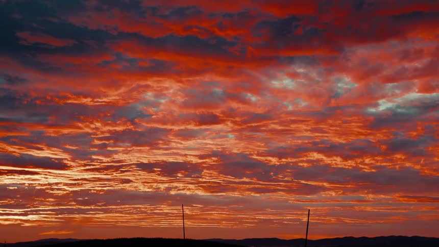 Utility poles across the landscape under a cloudy bright pink sunset sky