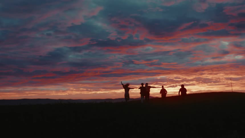 Friends running in an open field towards the horizon in the after glow of sunset