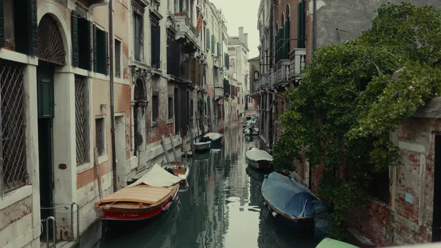 Covered gondolas parked in canal between backside of apartment buildings in venice