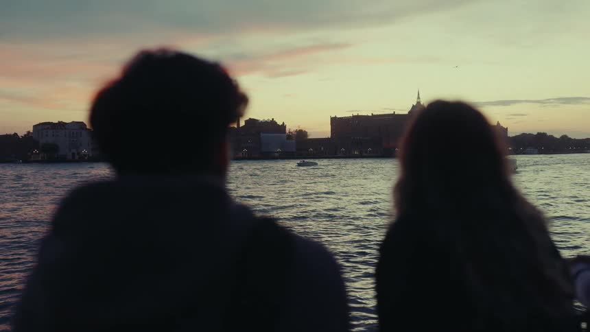 Silhouette of a man and a woman enjoying the view of the sea with a city in the background