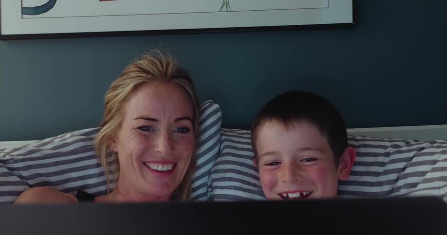 Mother and son laying in bed laughing watching a show from laptop