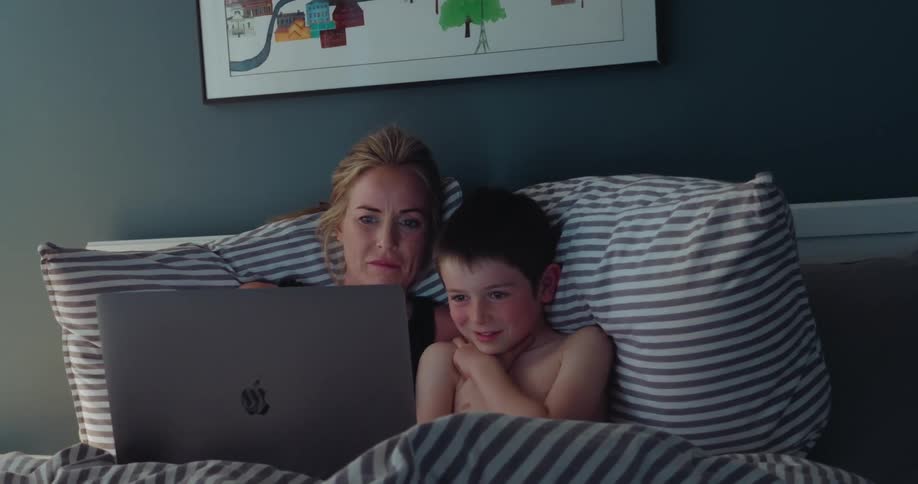 A mother and son watch the laptop in bed