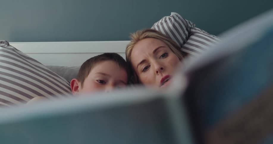 Mother lies in bed with her son while reading him a story
