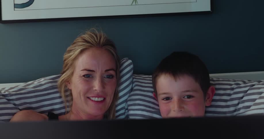 A woman and a child are in bed looking at a screen