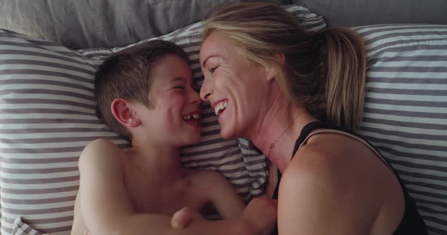 A mother and son laugh and talk in bed