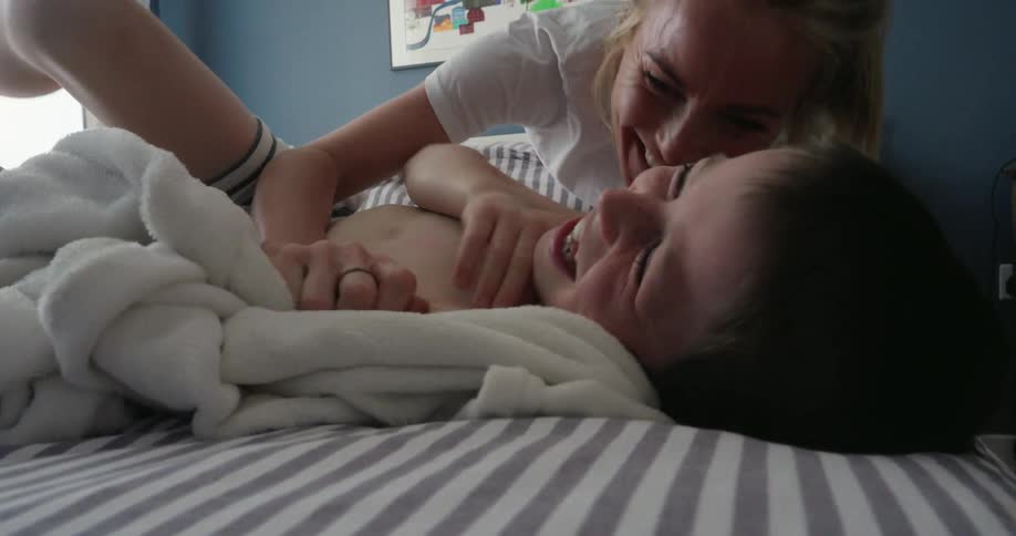 A mother and son laugh and play in the bedroom