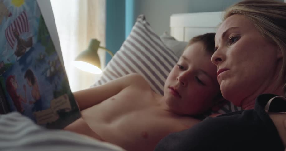 Mother reads a book to her son on the bed in the morning