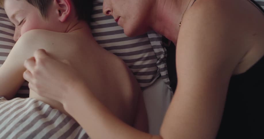 Mother strokes and scratches the back of her smiling son while they lie on a bed