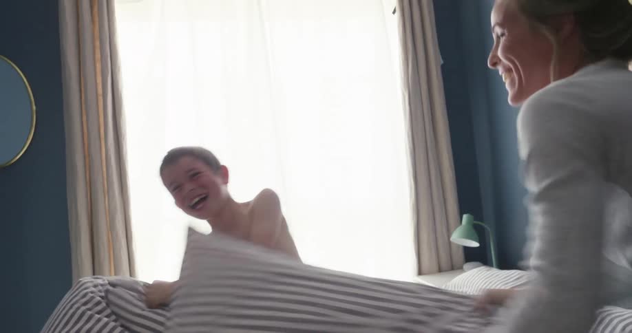 Mother and son laughing having a pillow fight on the bed in the morning