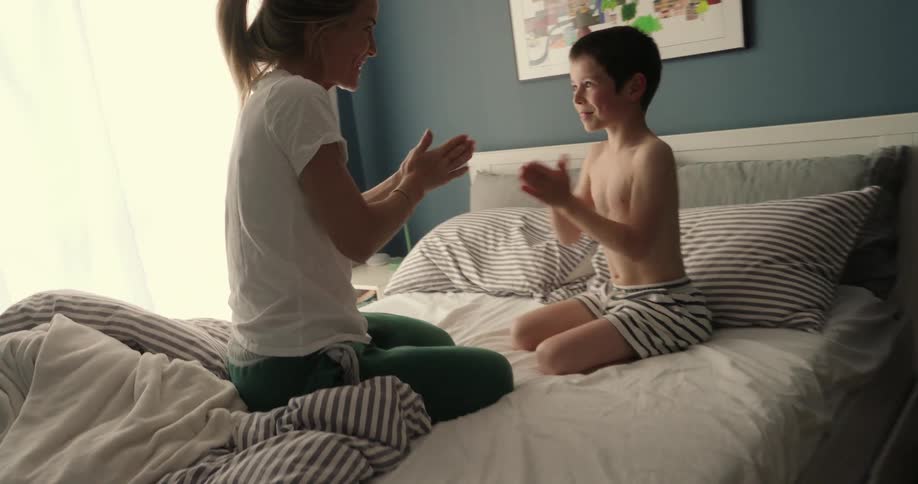 Mother and son sitting on the bed playing patty cakes in the morning
