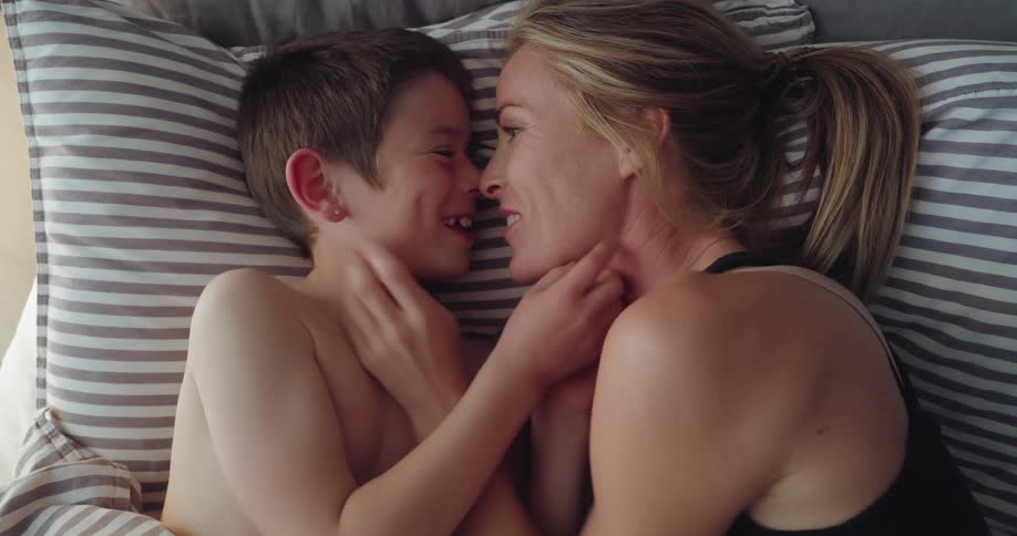 Boy tries to tickle his mother while the two lie on a bed during the daytime