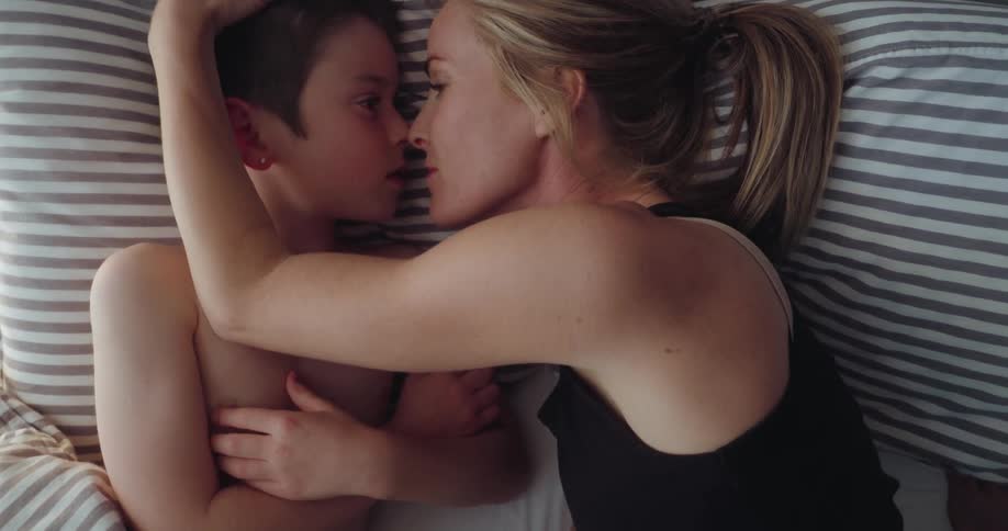 Woman and child exchange affectionate glances as they lie side by side in bed