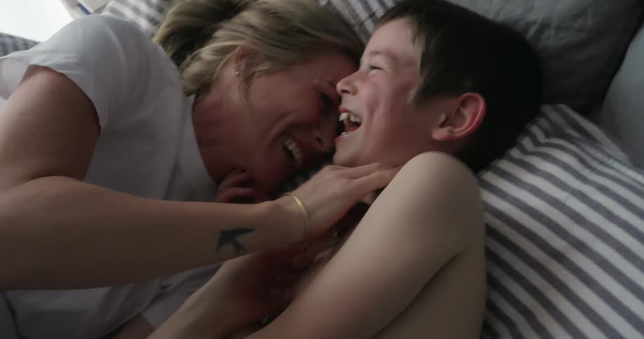 A mother is tickling her son in bed