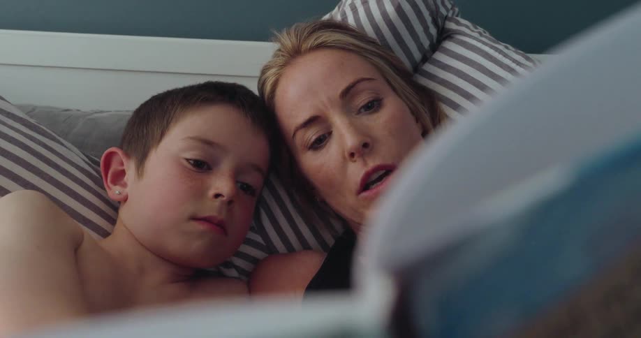 Mother lying with her son in bed reading a book