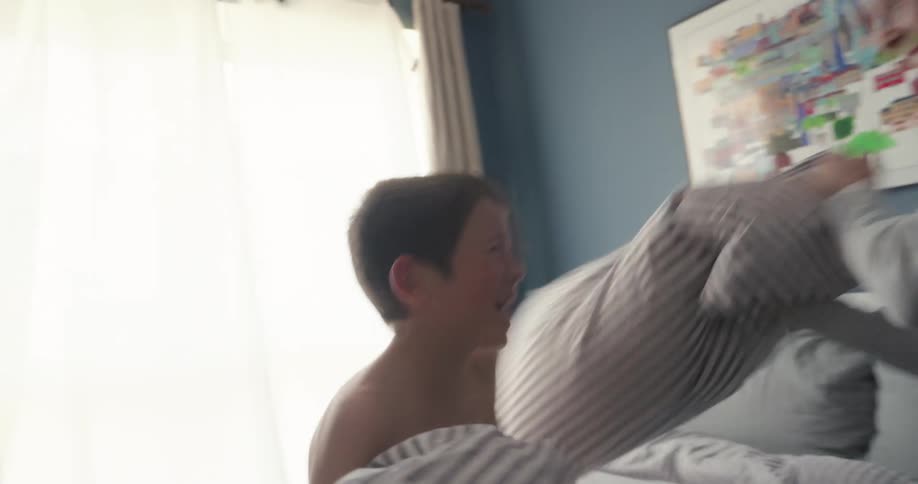 A mother and her son have a pillow fight while sitting in bed