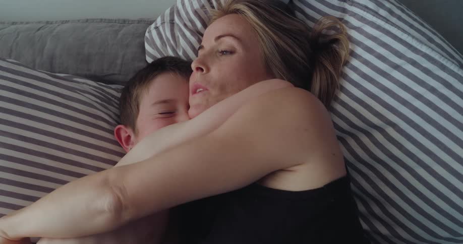 Mother is hugging her son while laying in bed