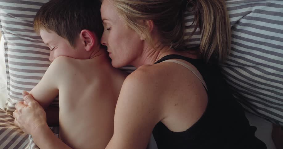 Woman cuddles her son while sleeping on the bed in the morning
