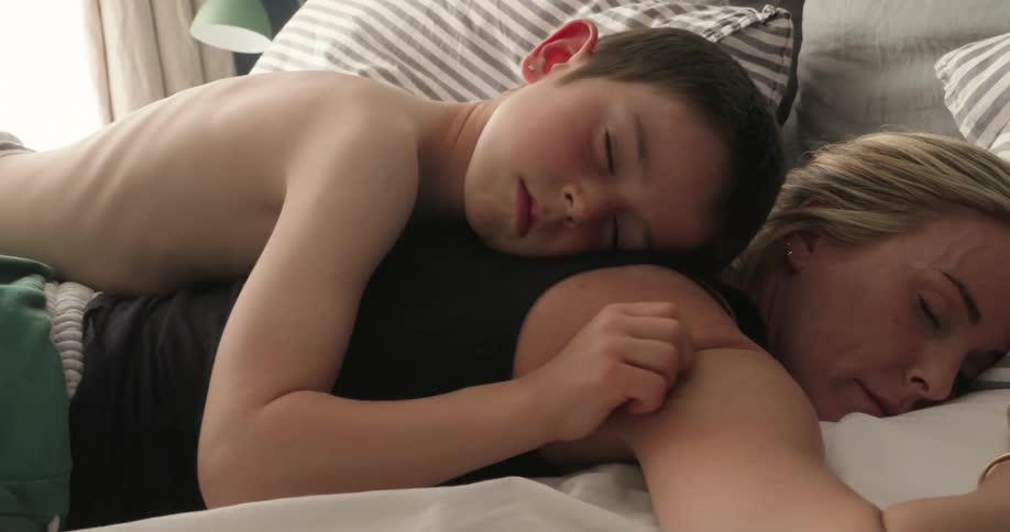 A young boy sleeps closely beside a woman softly scratching her arm in a calm tender moment