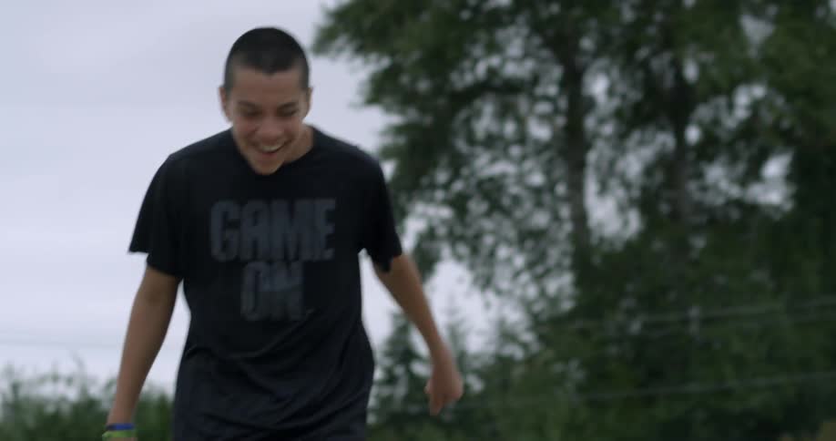 A teenage boy is laughing as he picks up a football from the ground