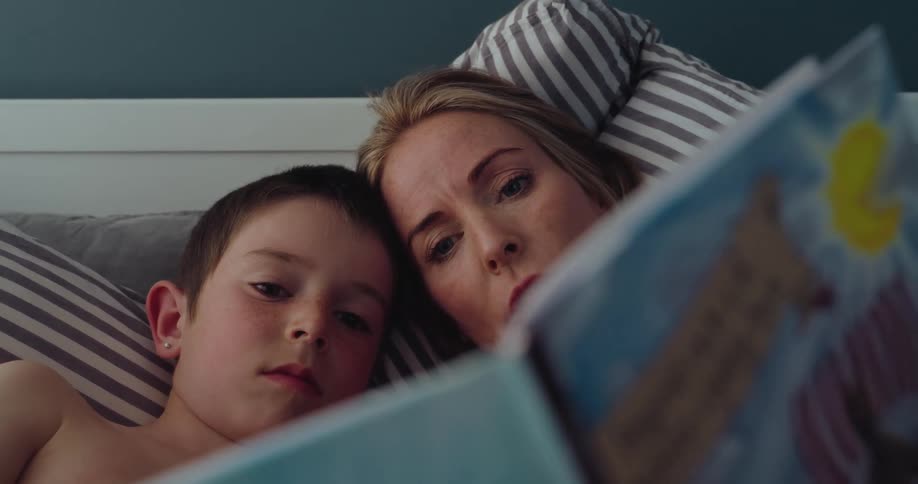 Mother laying in bed with her son as she reads to him from a book