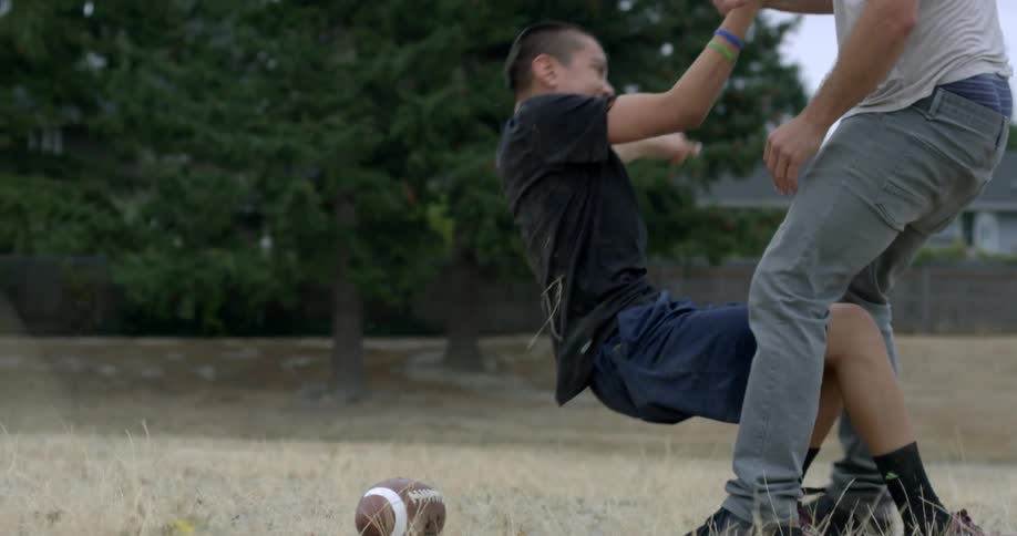 A man helps a boy up from the ground with a football nearby